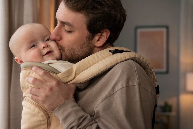 Medium shot father holding cute baby in carrier