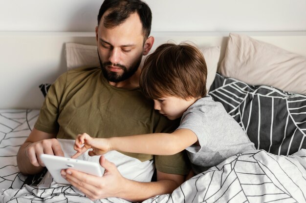 Medium shot father and son in bed with device