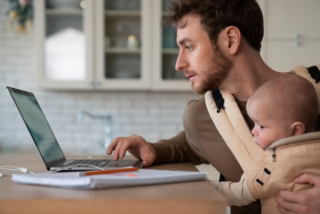 Medium shot father working while holding baby