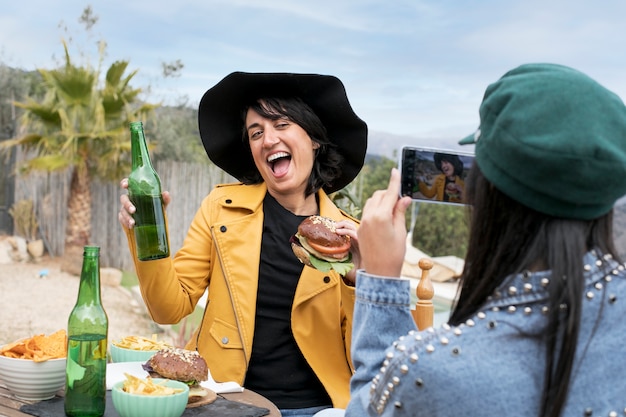 Free photo medium shot friend taking photos of woman with burger