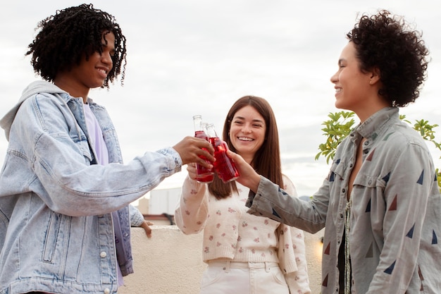 Free photo medium shot friends clinking bottles