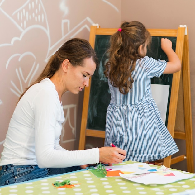 Free photo medium shot girl drawing on chalkboard