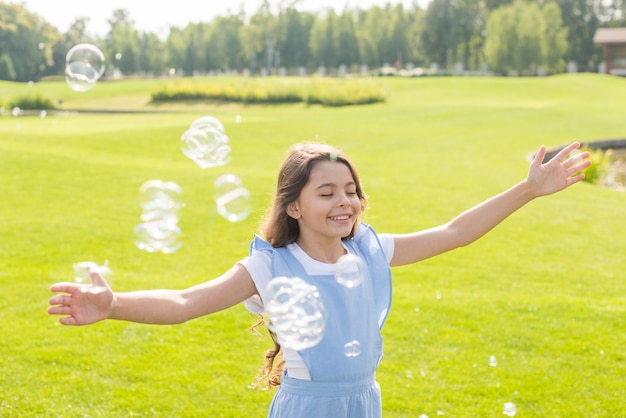 Foto gratuita ragazza del colpo medio che gioca con le bolle di sapone all'aperto