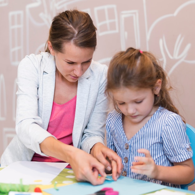 Medium shot girl and teacher gluing paper