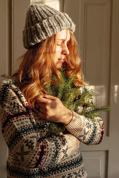 Medium shot girl with hat holding fir tree twigs