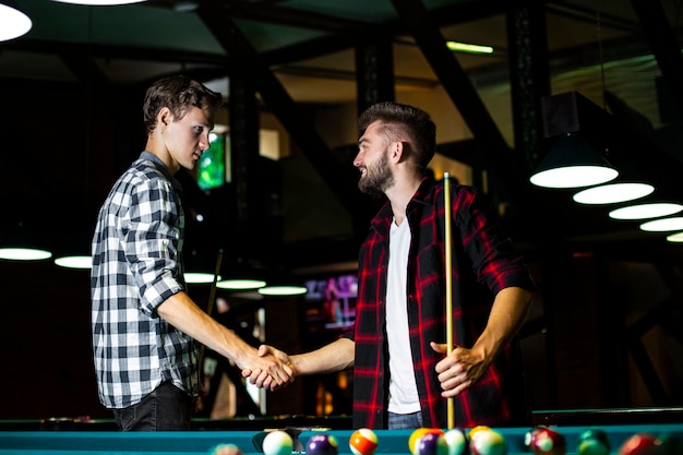 Medium shot guys shaking hands near pool table