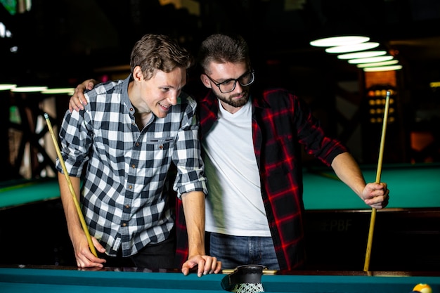 Medium shot guys with pool cues near pool table