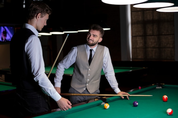 Medium shot guys with vests near billiard table 