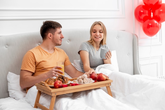 Medium shot happy couple having breakfast in bedroom