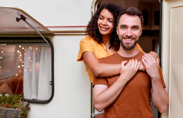 Medium shot of happy  couple standing in front of camper van
