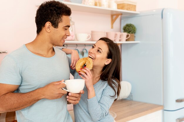 Medium shot happy couple with doughnut and cup