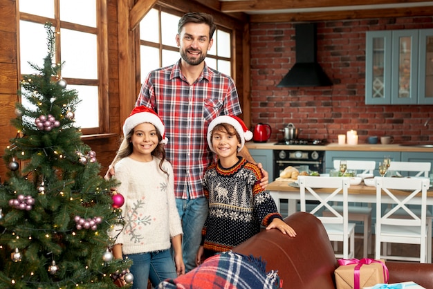 Medium shot happy family posing near christmas tree