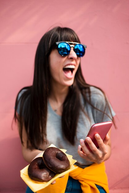 Medium shot happy girl with doughnuts and smartphone