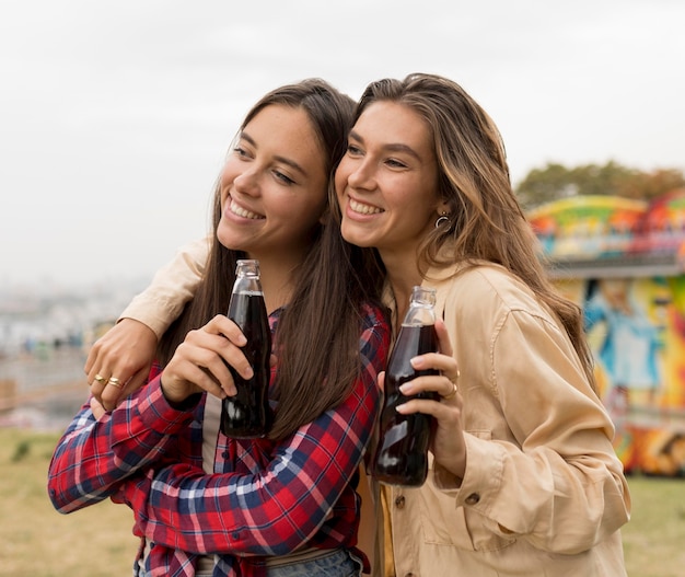 Medium shot happy girls holding soda bottles