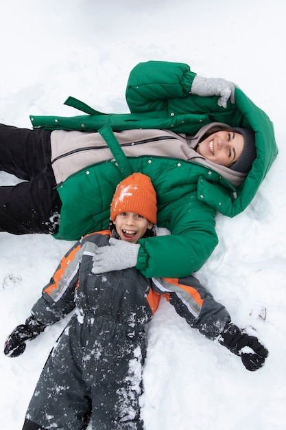 雪の中で横たわっているミディアムショットの幸せな子供と女性