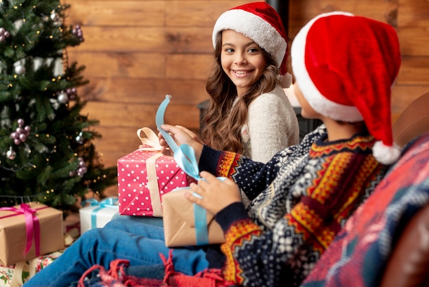 Medium shot happy kids with gifts near the christmas tree