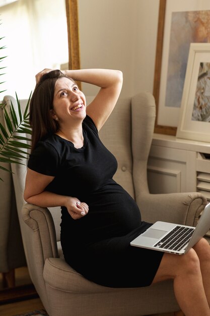 Medium shot happy pregnant woman with laptop