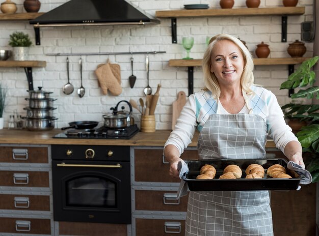 Medium shot happy woman carrying tray with croissants