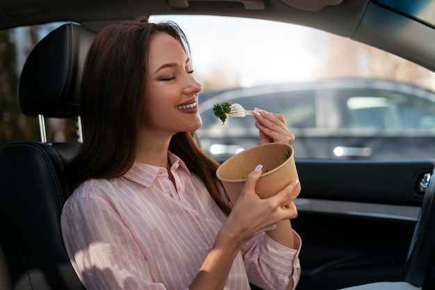 Free photo medium shot healthy woman eating in car