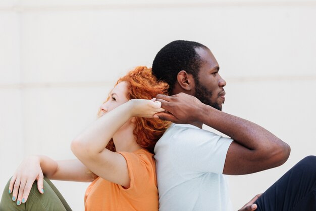 Medium shot of interracial couple back to back holding hands