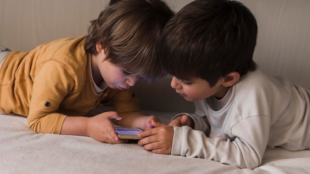 Medium shot kids in bed with smartphone