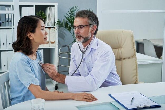 Medium shot of male doctor examining the female patient with stethoscope