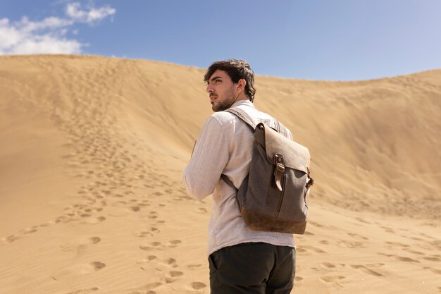 Medium shot man carrying backpack in desert