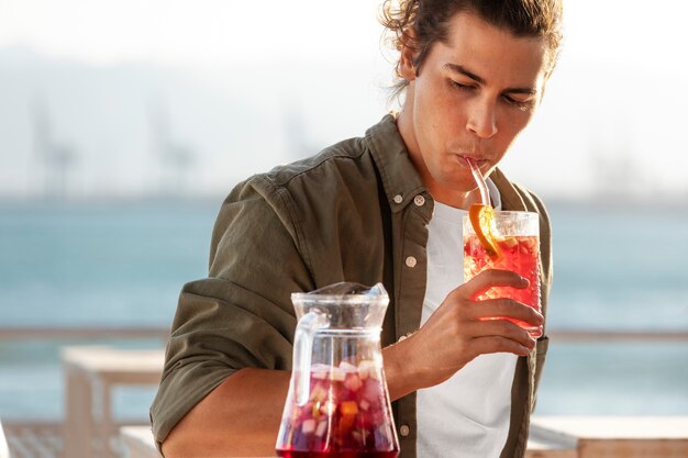 Medium shot man drinking sangria at seaside