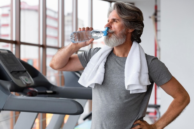 Medium shot man drinking water at gym