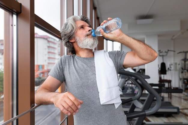 ミディアムショットの男がジムで水を飲む