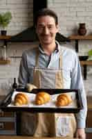 Free photo medium shot man holding croissants tray