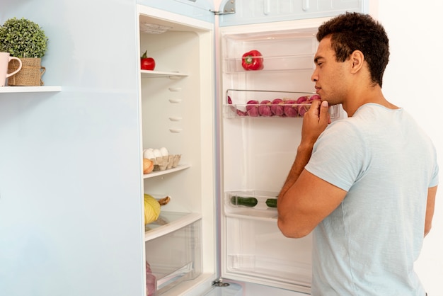 Free photo medium shot man looking in the fridge