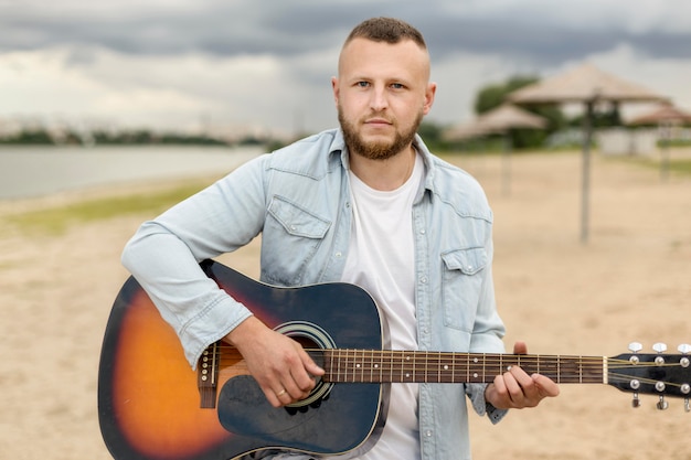 medium shot man playing the guitar on a beach