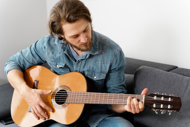 Uomo del colpo medio che gioca chitarra sul divano