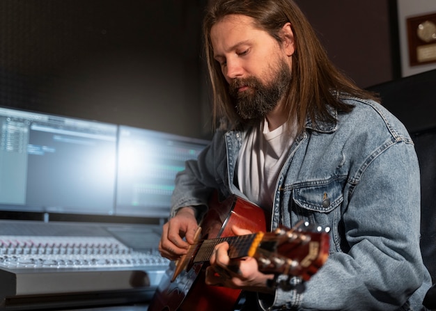 Medium shot man playing the guitar in studio