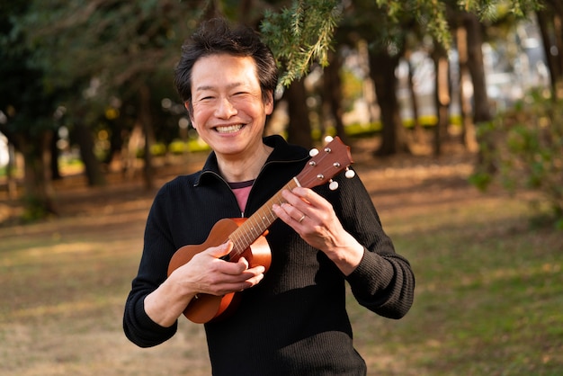 Foto gratuita uomo del tiro medio che suona l'ukulele all'esterno