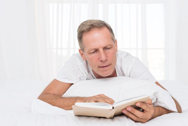 Medium shot man reading in the bedroom