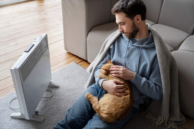 Free photo medium shot man with cat near heater