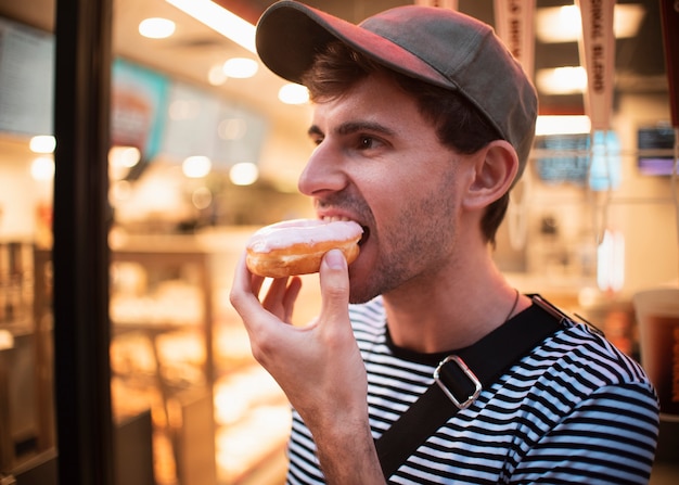 Free photo medium shot man with hat eating doughnut