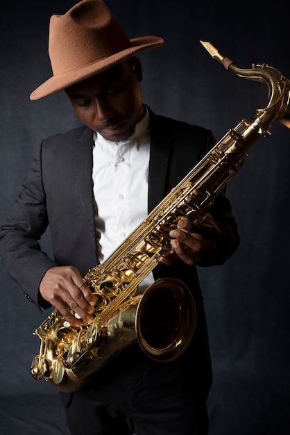 Medium shot man with hat holding saxophone