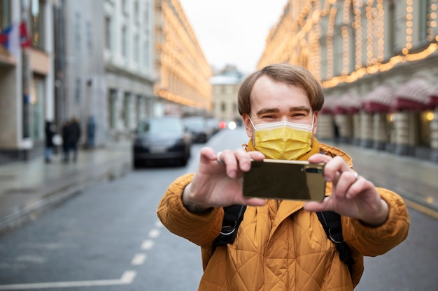 Medium shot man with mask taking selfie