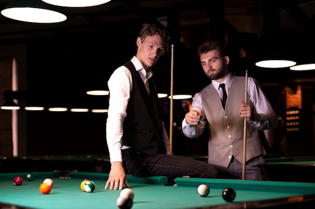 Medium shot men with vests near pool table 