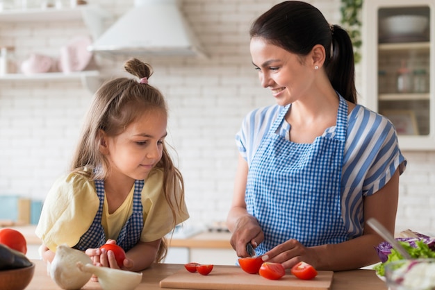 Free photo medium shot mother cutting tomatoes