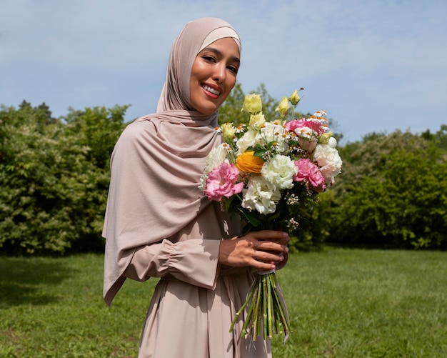 花とポーズをとるミディアムショットのイスラム教徒の女性