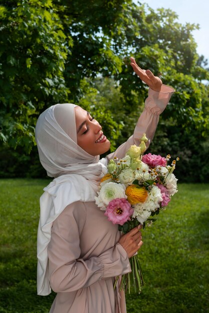 꽃과 함께 포즈를 취하는 중간 샷 이슬람 여성