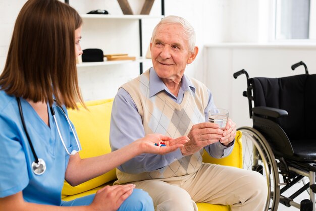 Medium shot nurse giving an old man his pills 