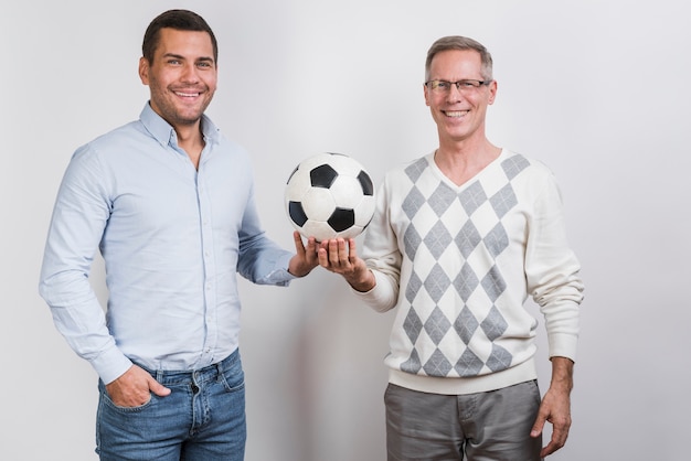 Бесплатное фото Средний снимок отца и сына, держащего футбольный мяч