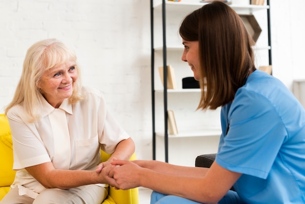 medium shot old woman and nurse holding hands 