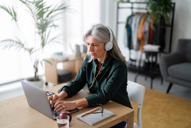 Medium shot old woman with headphones at desk