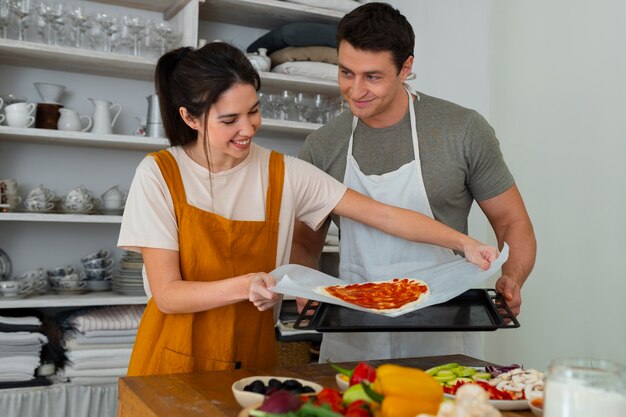 Medium shot people cooking pizza together